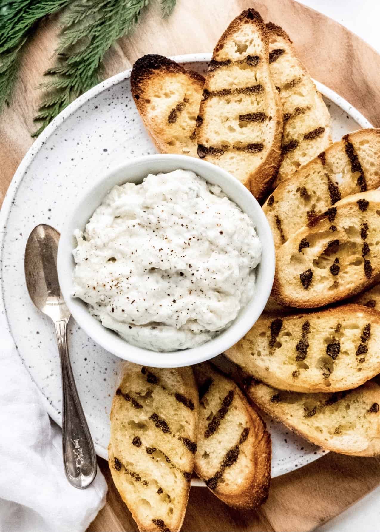 white bean artichoke dip in bowl surrounded by grilled baguette slices