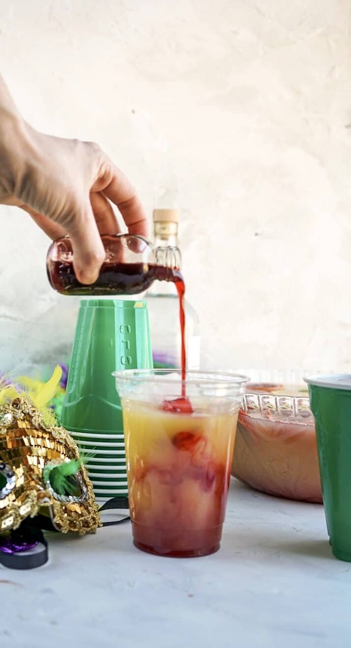 Hurricane Punch bowl pouring blood orange syrup in cup of Hurricane Punch