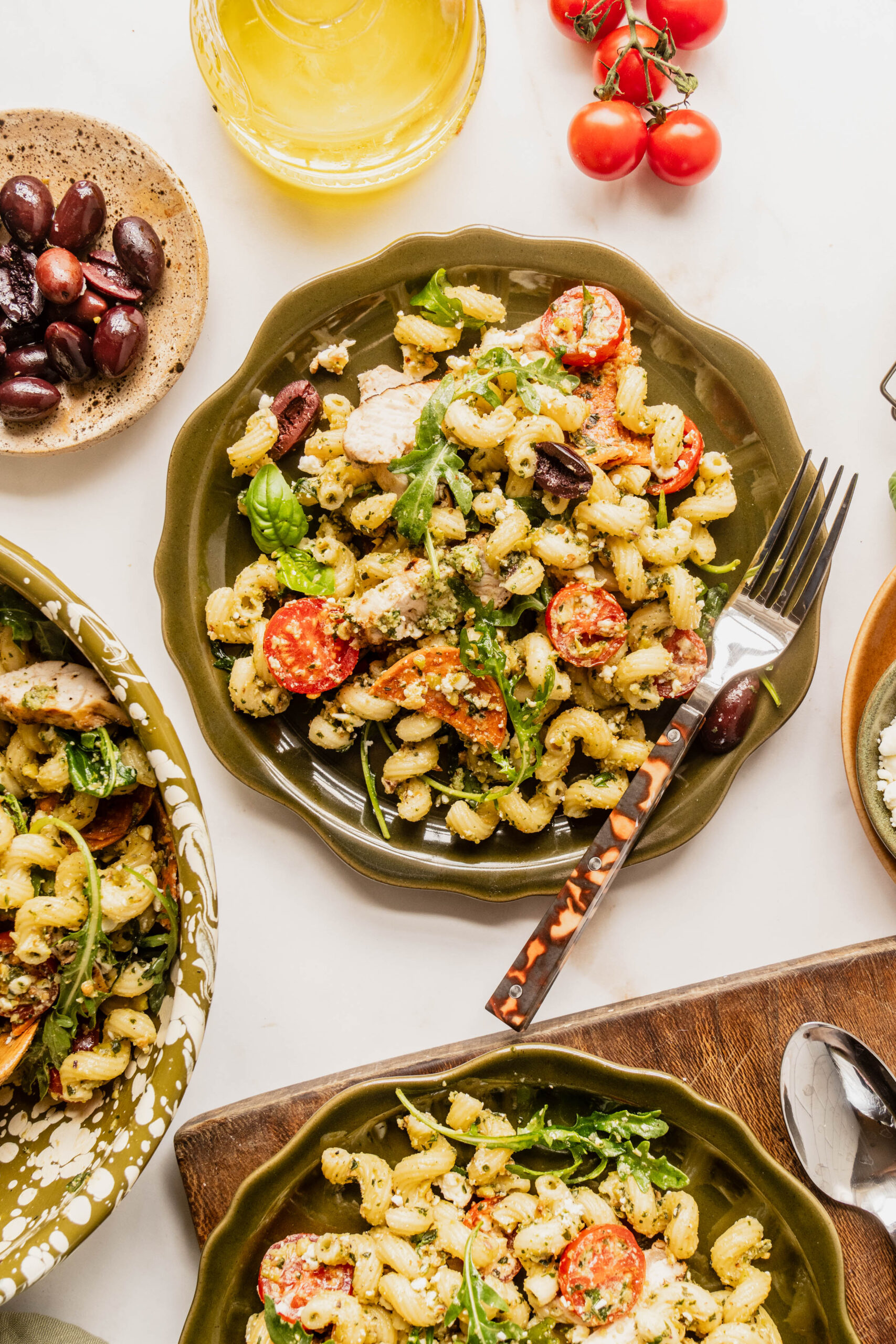Overhead view of pasta salad pesto chicken served in individual bowls with corkscrew pasta tossed in basil pesto, sliced grilled chicken, cherry tomatoes, kalamata olives, feta cheese, and fresh arugula, styled on a light marble surface.Select 64 more words to run Humanizer.