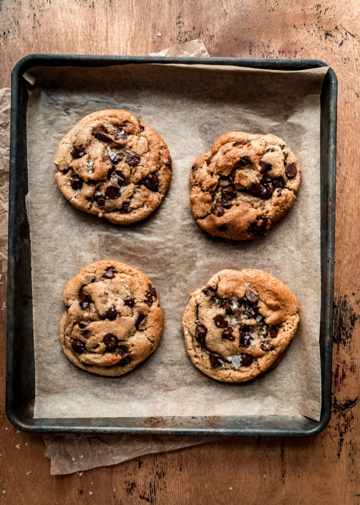 overhead shot of four chocolate chip cookies on baking sheet with brown parchment paper underneath