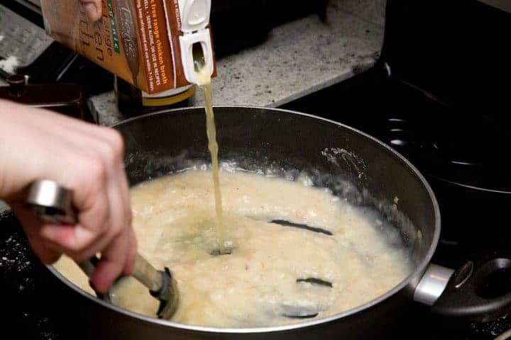 Chicken stock for healthy chicken piccata sauce being poured into saute pan on stove.