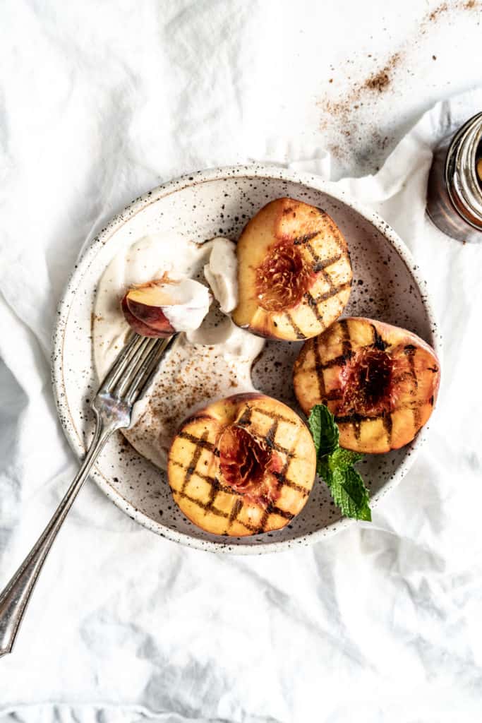 grilled peaches in a bowl with mascarpone cream and fork garnished with mint