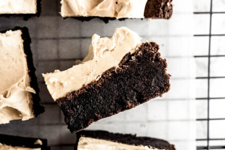 Fudgy chocolate brownies topped with creamy peanut butter whiskey frosting arranged on a wire cooling rack, with one brownie lifted to show the dense, rich chocolate center and smooth peanut butter whiskey buttercream.