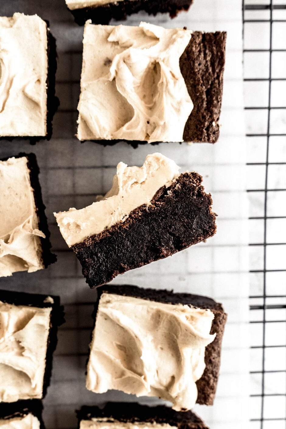 Fudgy chocolate brownies topped with creamy peanut butter whiskey frosting arranged on a wire cooling rack, with one brownie lifted to show the dense, rich chocolate center and smooth peanut butter whiskey buttercream.