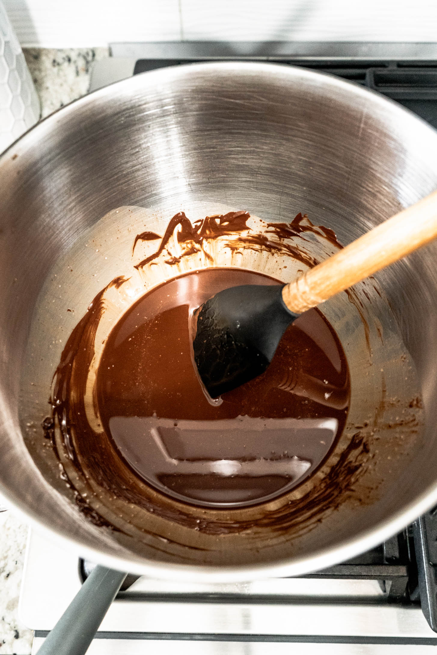 Melted chocolate and butter being stirred in a metal bowl over a stovetop while preparing peanut butter whiskey brownies.