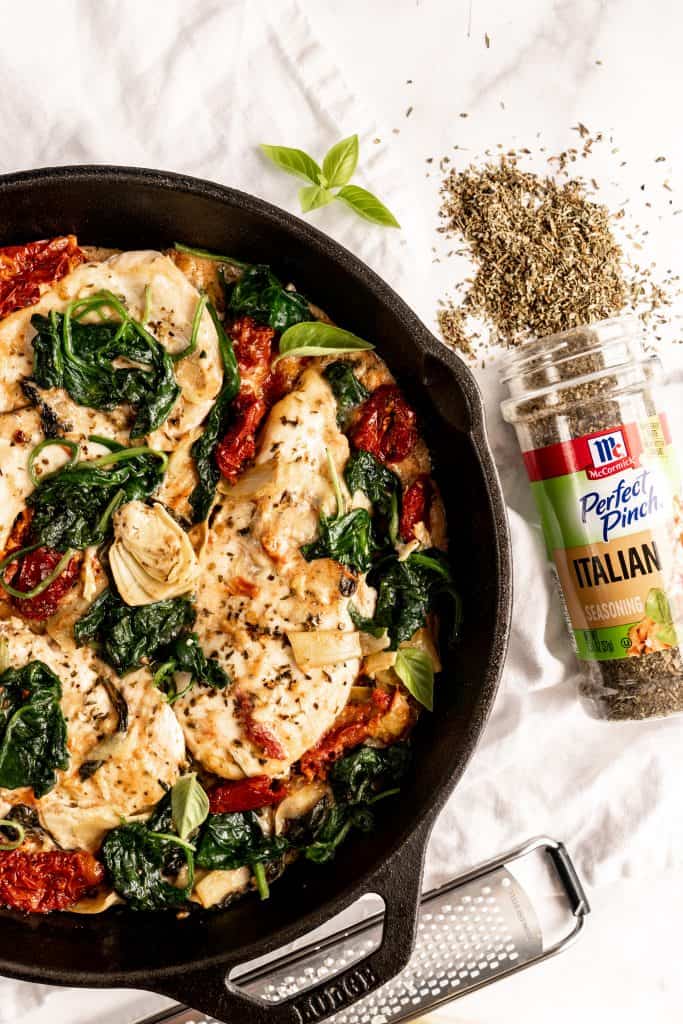 finished creamy tuscan chicken in skillet with seasoning bottle and herbs spilling out