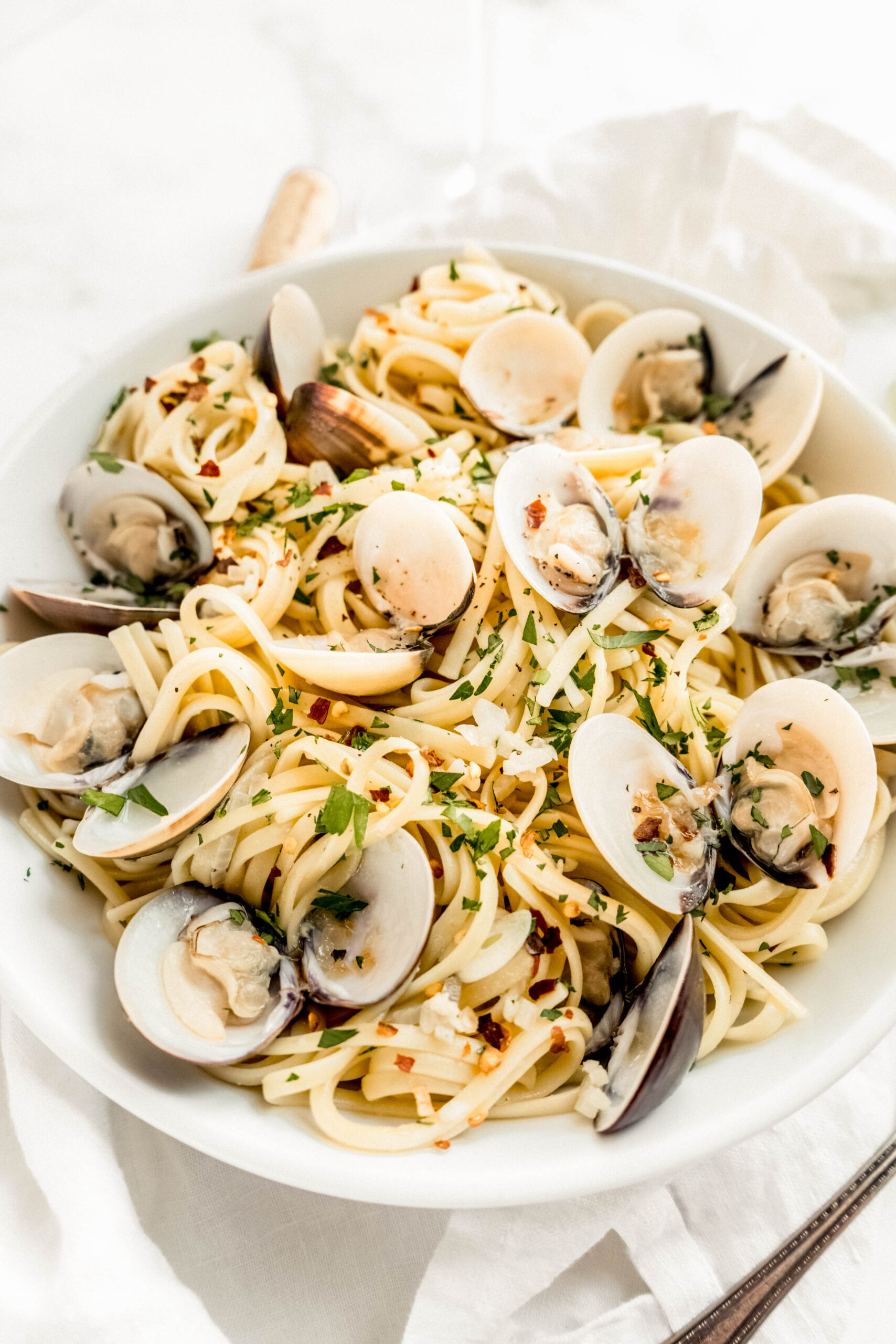 Linguine with clams in white wine sauce served in a white bowl, featuring tender linguine tossed with garlic, olive oil, and lemon, topped with opened clams, fresh parsley, and red pepper flakes.