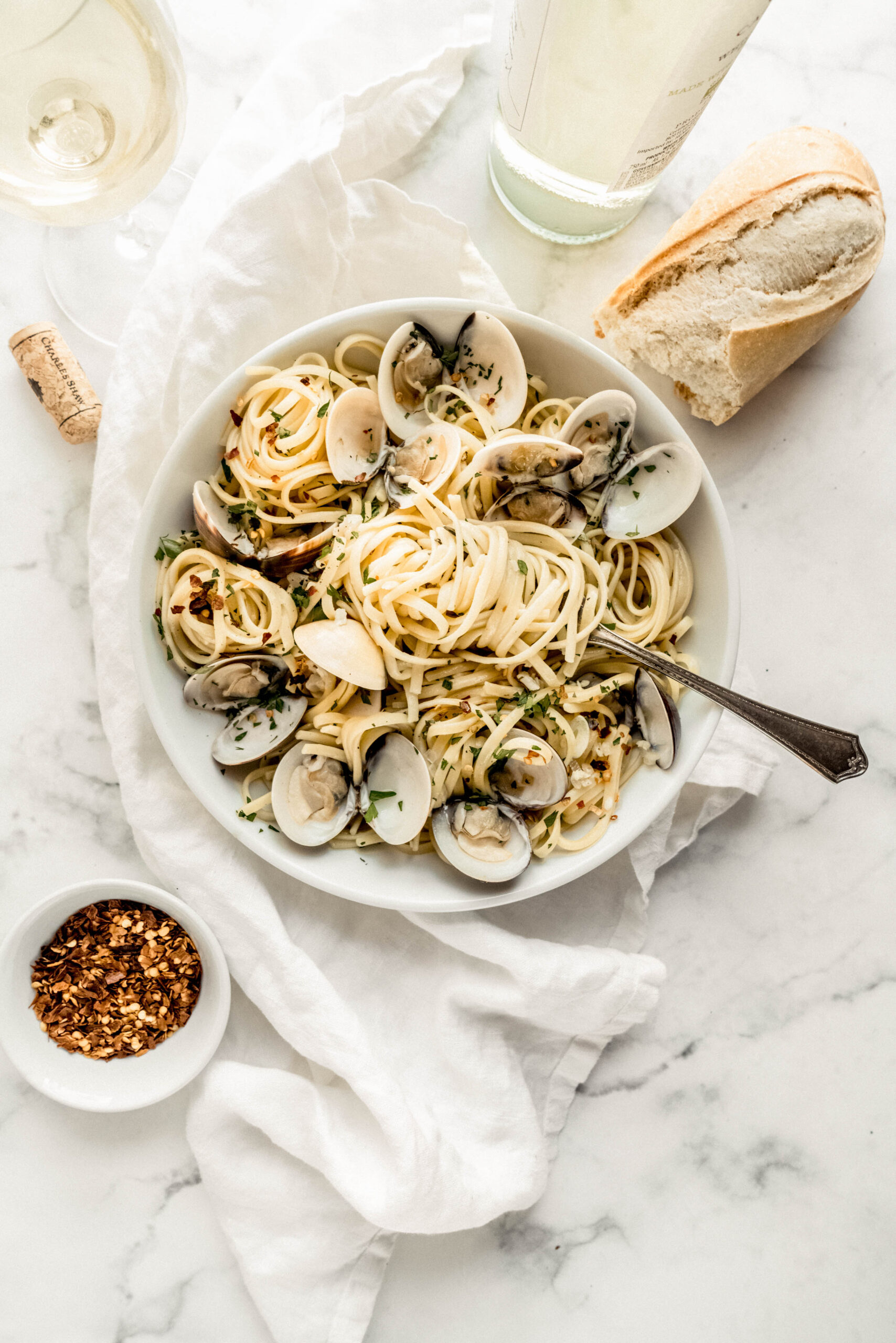 Linguine with clams in white wine sauce served in a white bowl, with tender pasta and opened clams tossed in a garlic white wine sauce, garnished with fresh parsley and red pepper flakes, and paired with crusty bread and a glass of white wine.