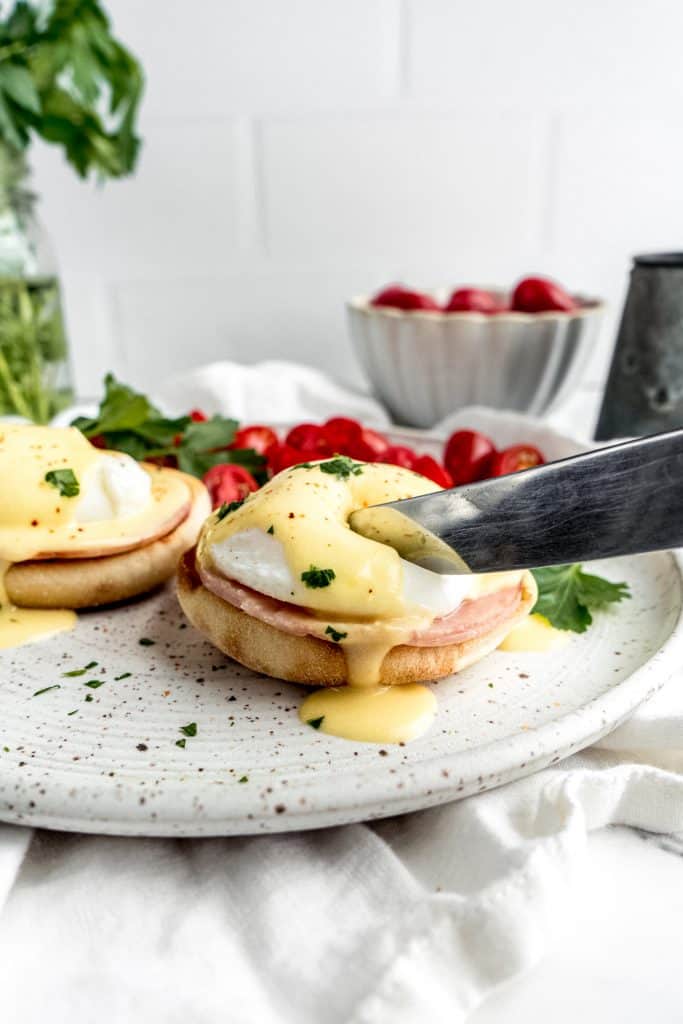 eggs benedict with citrus hollandaise plated and knife cutting into the egg