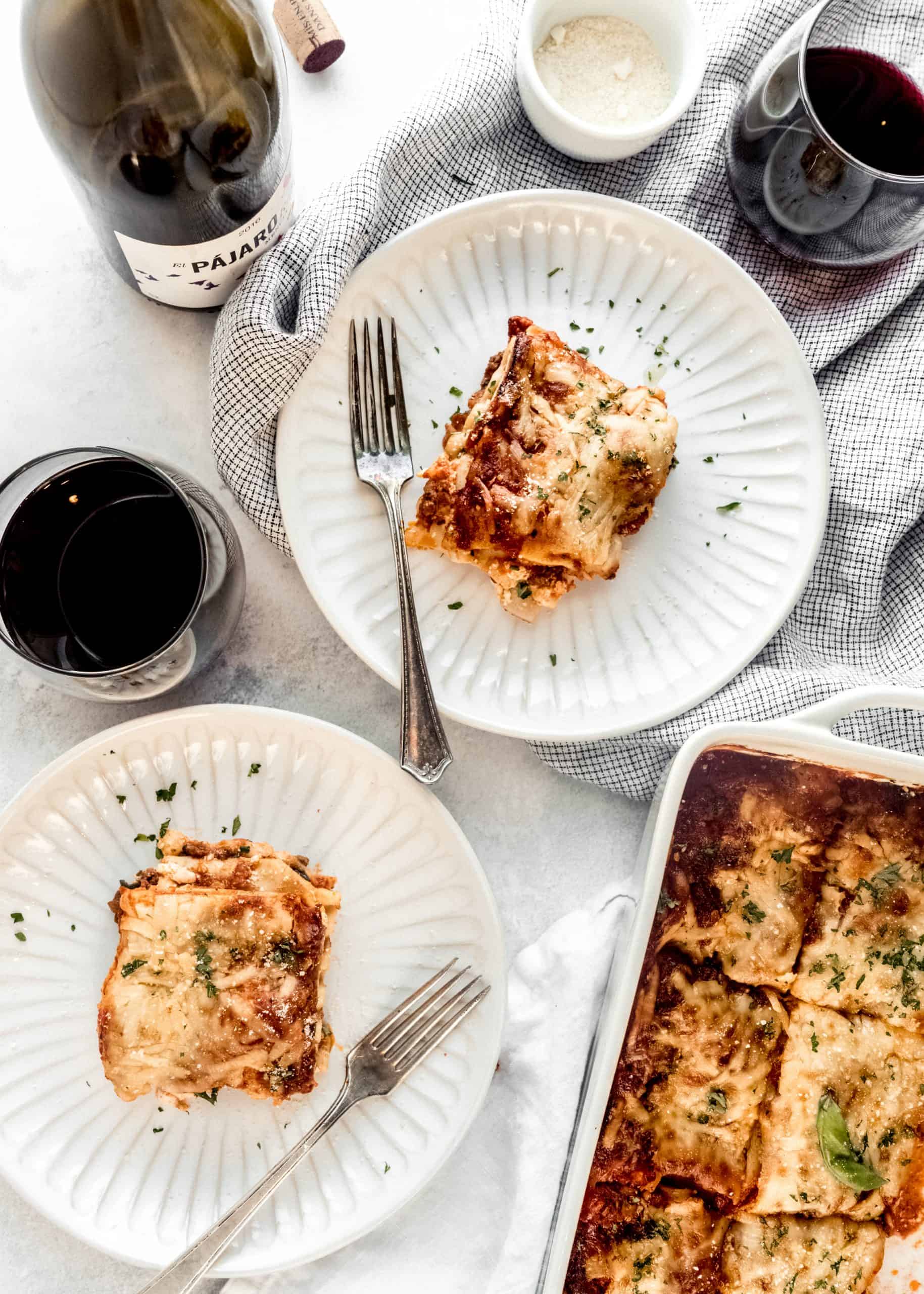 pieces of lasagna on plates with glass of red wine