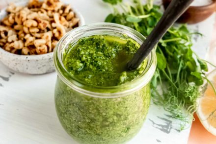 pea shoot pesto in a jar with walnuts and raw pea shoots surrounding it