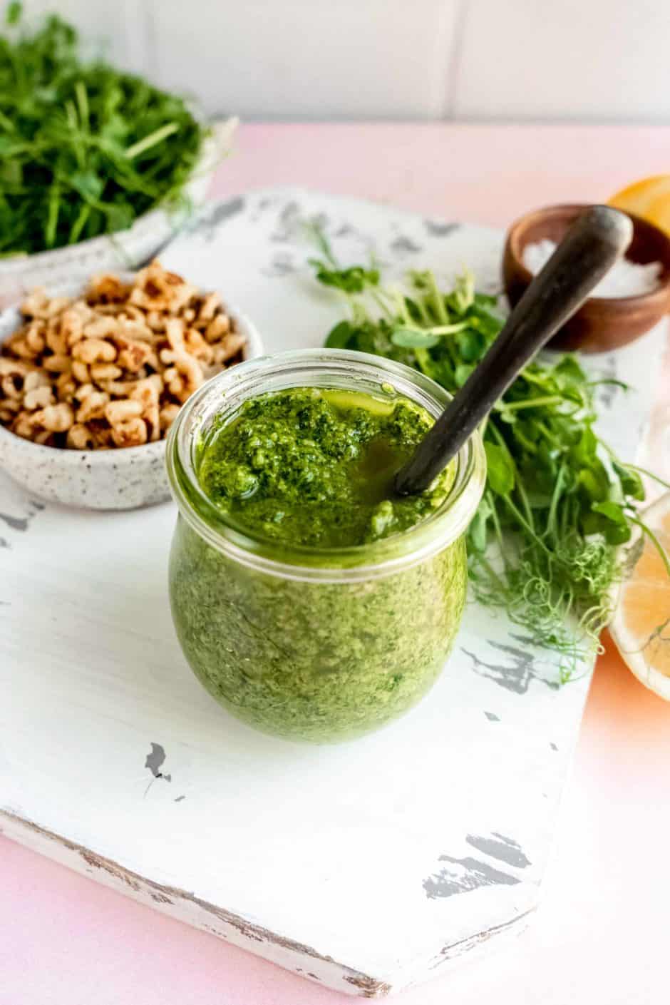 pea shoot pesto in a jar with walnuts and raw pea shoots surrounding it