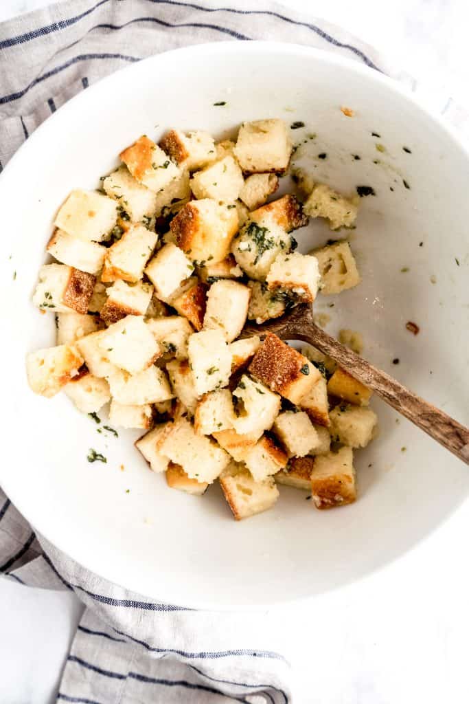 cubed bread tossed in olive oil and herbs in white bowl