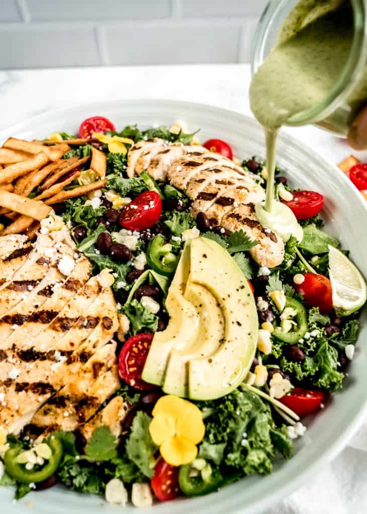 cilantro dressing being poured on chicken in grilled chicken taco salad