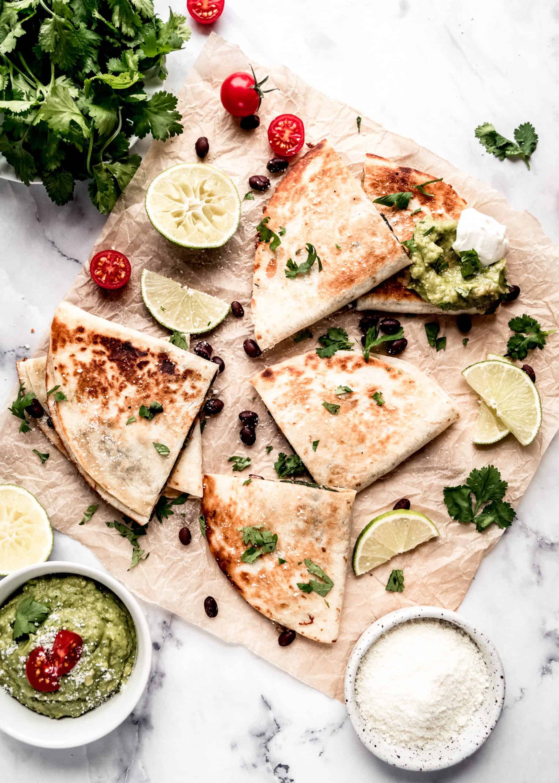 quesadillas on parchment paper garnished with guacamole and sour cream