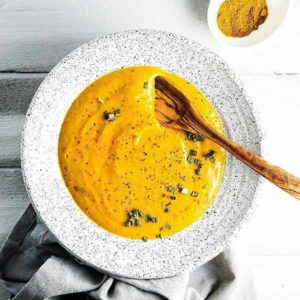 Top view of soup in a speckled white pasta bowl with a wooden spoon in it