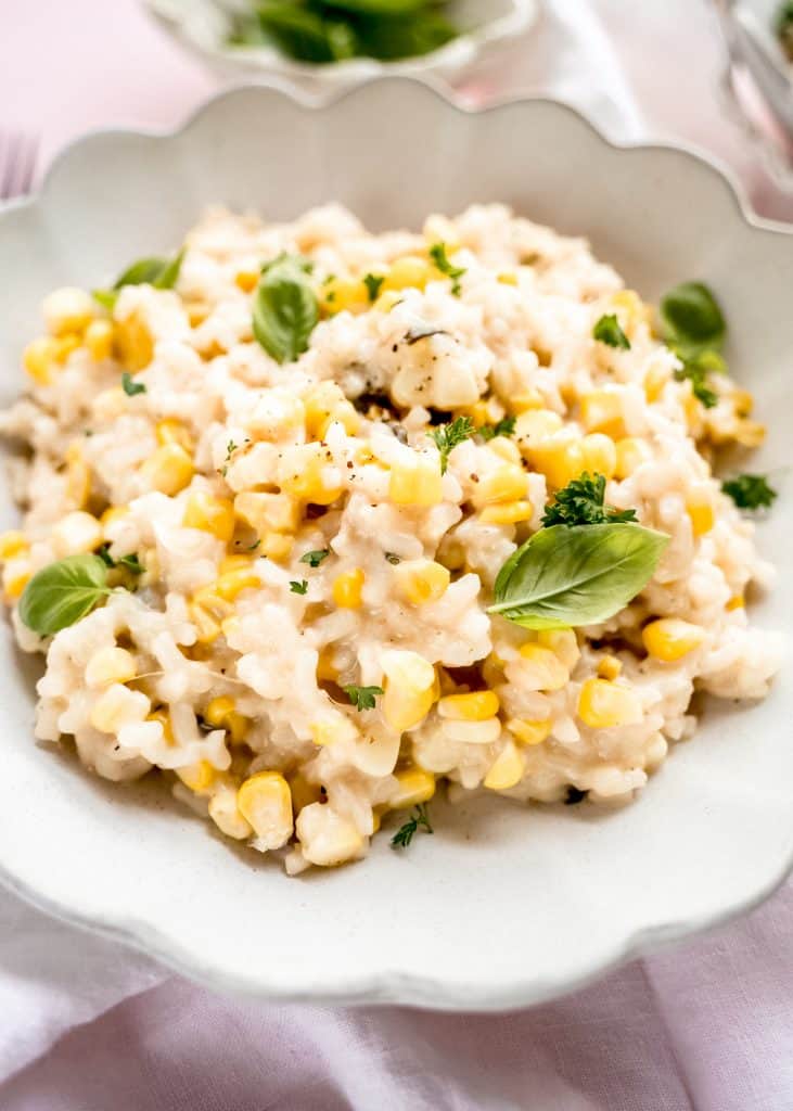 close up shot of sweet corn risotto in bowl garnished with basil