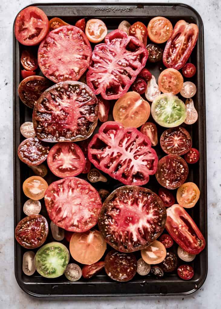 raw heirloom tomatoes sliced in half on sheet pan