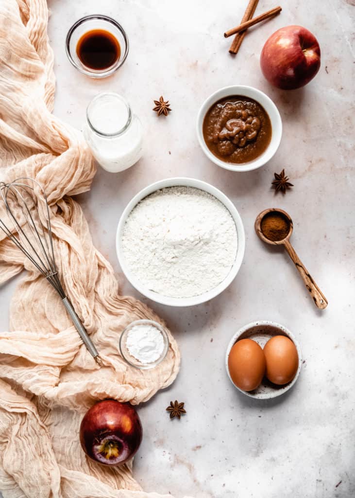 apple butter waffle ingredients in bowls on backdrop, whole apples and cinnamon sticks laying next to bowls