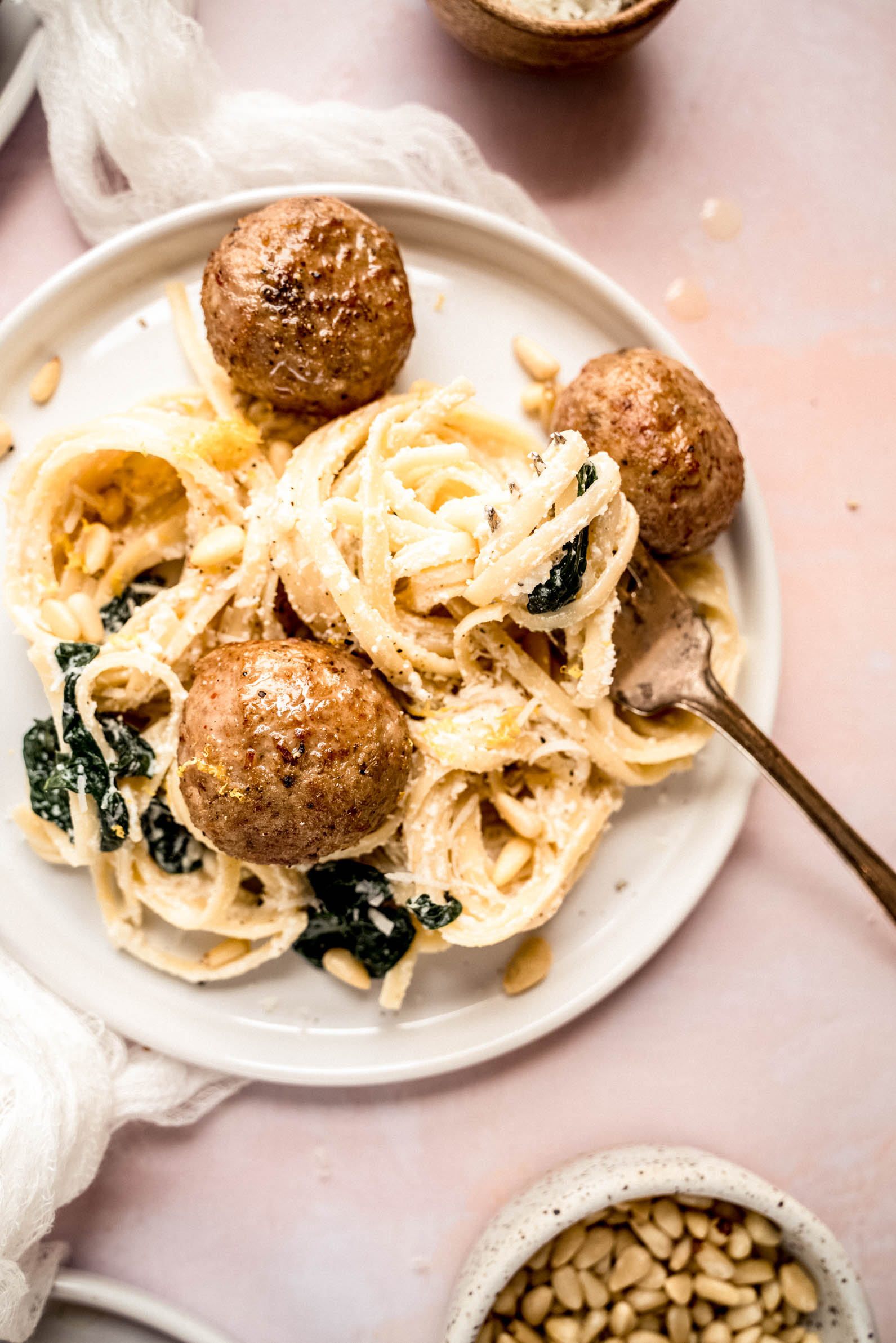 Lemon ricotta pasta recipe served on a white plate with creamy linguine tossed in ricotta sauce, wilted spinach, toasted pine nuts, and topped with juicy meatballs, styled in a warm, bright overhead food photography shot.