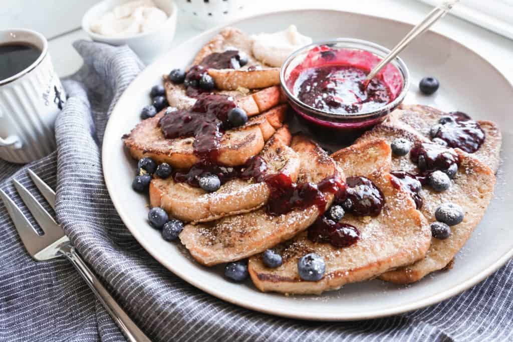 close up shot of fluffy french toast in serving dish with berry sauce, garnished with blueberries and whipped mascarpone