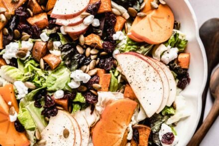 Persimmons salad recipe in a scalloped bowl with maple vinaigrette in glass jar next to bowl.