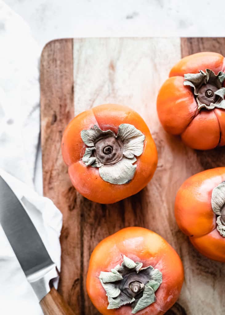 up close shot of whole fresh persimmons on wood cutting board