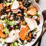 Persimmons salad recipe in a scalloped bowl with maple vinaigrette in glass jar next to bowl.
