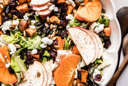 Persimmons salad recipe in a scalloped bowl with maple vinaigrette in glass jar next to bowl.