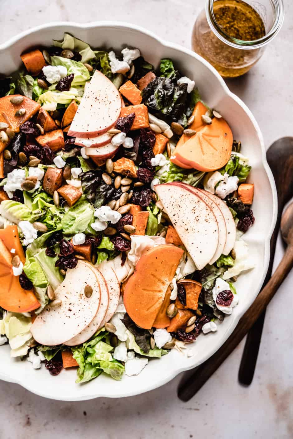 Persimmons salad recipe in a scalloped bowl with maple vinaigrette in glass jar next to bowl.