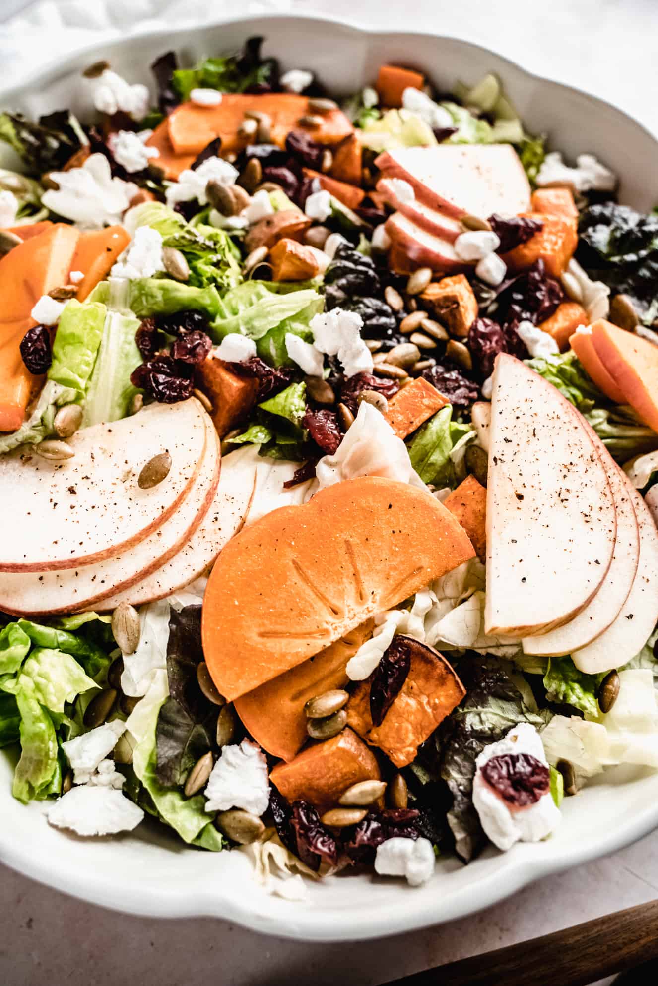 up close shot of sliced apples and sliced fresh persimmons on top of salad in bowl