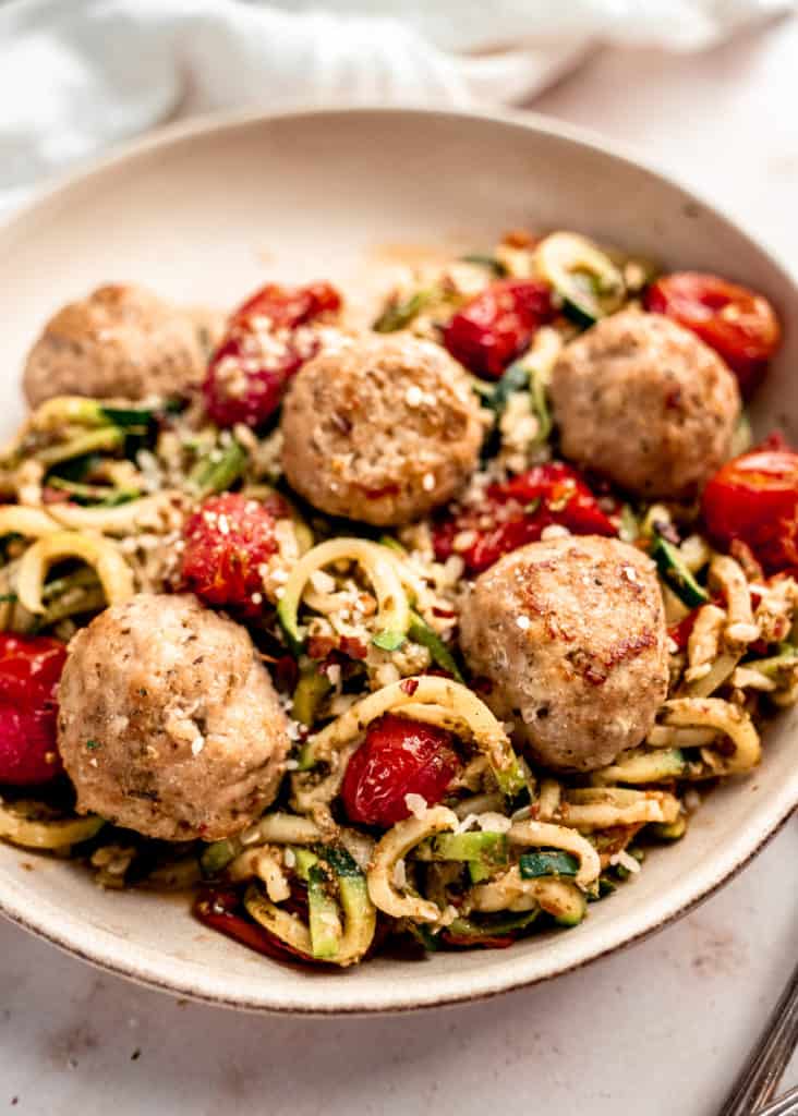 close up shot of baked meatballs and pesto zucchini noodles in bowl
