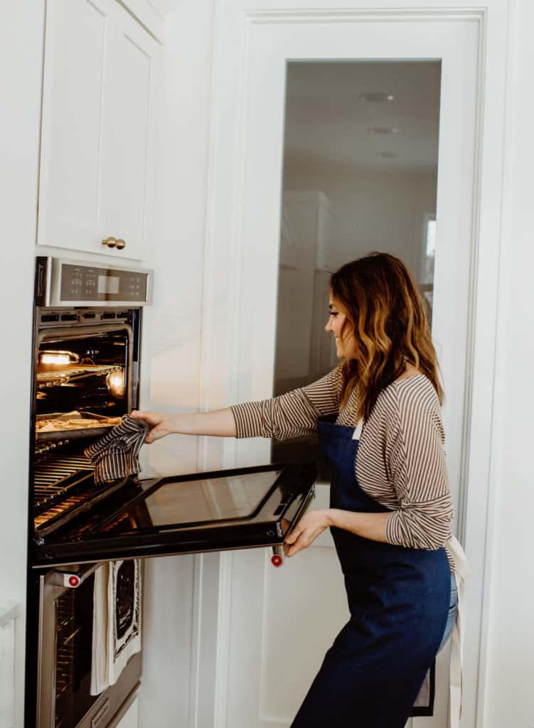 Nicole Tingwall pulling Chewy Oatmeal Chocolate Chip Cookies from the oven in a bright white kitchen