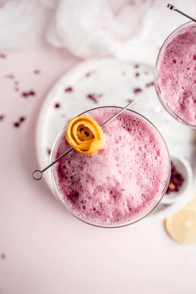 overhead shot of beet ginger beer mocktail in coupe glass on marble serving platter garnished with lemon rosette