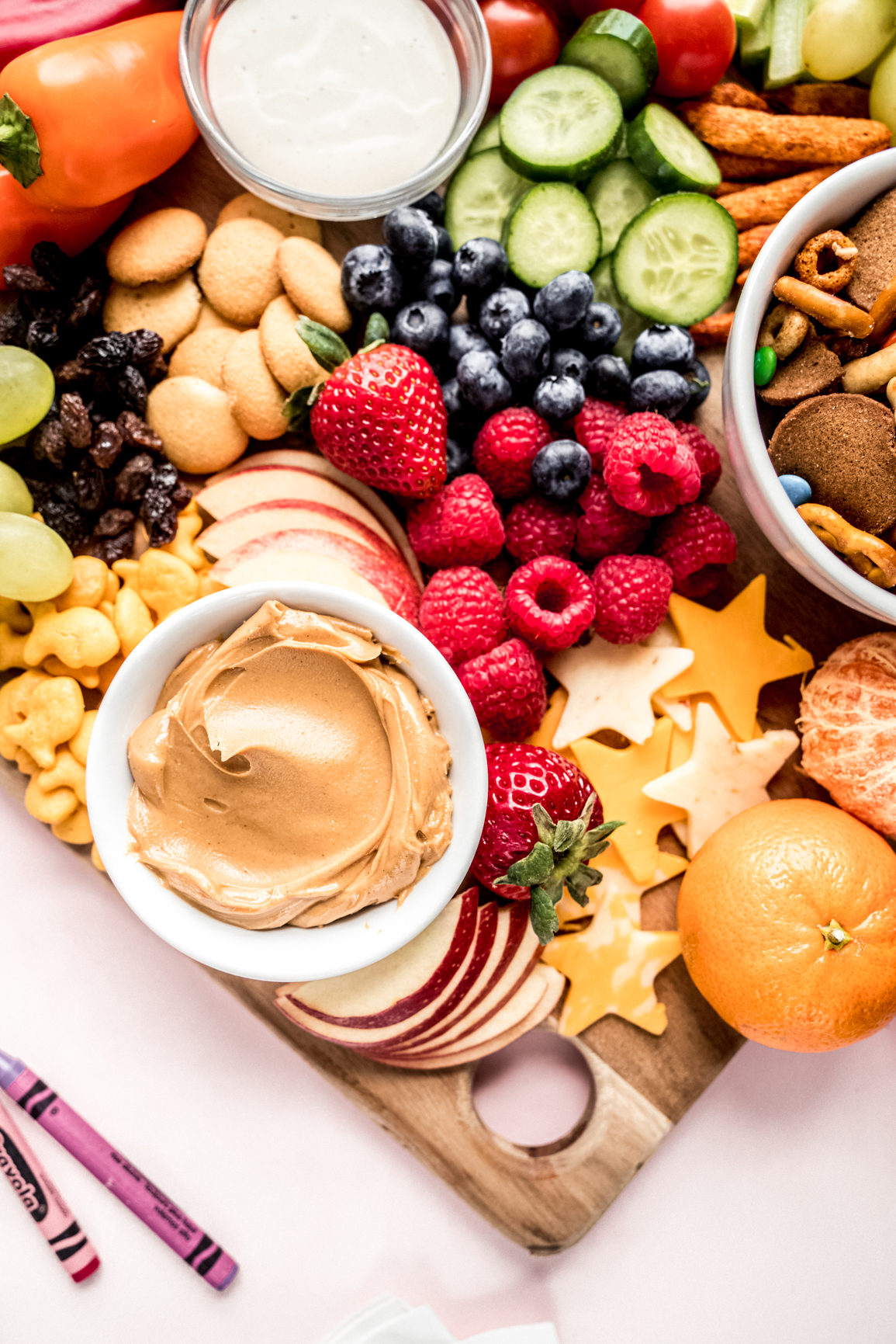 close up shot of peanut butter in small bowl surrounded by fruit on kids charcuterie board
