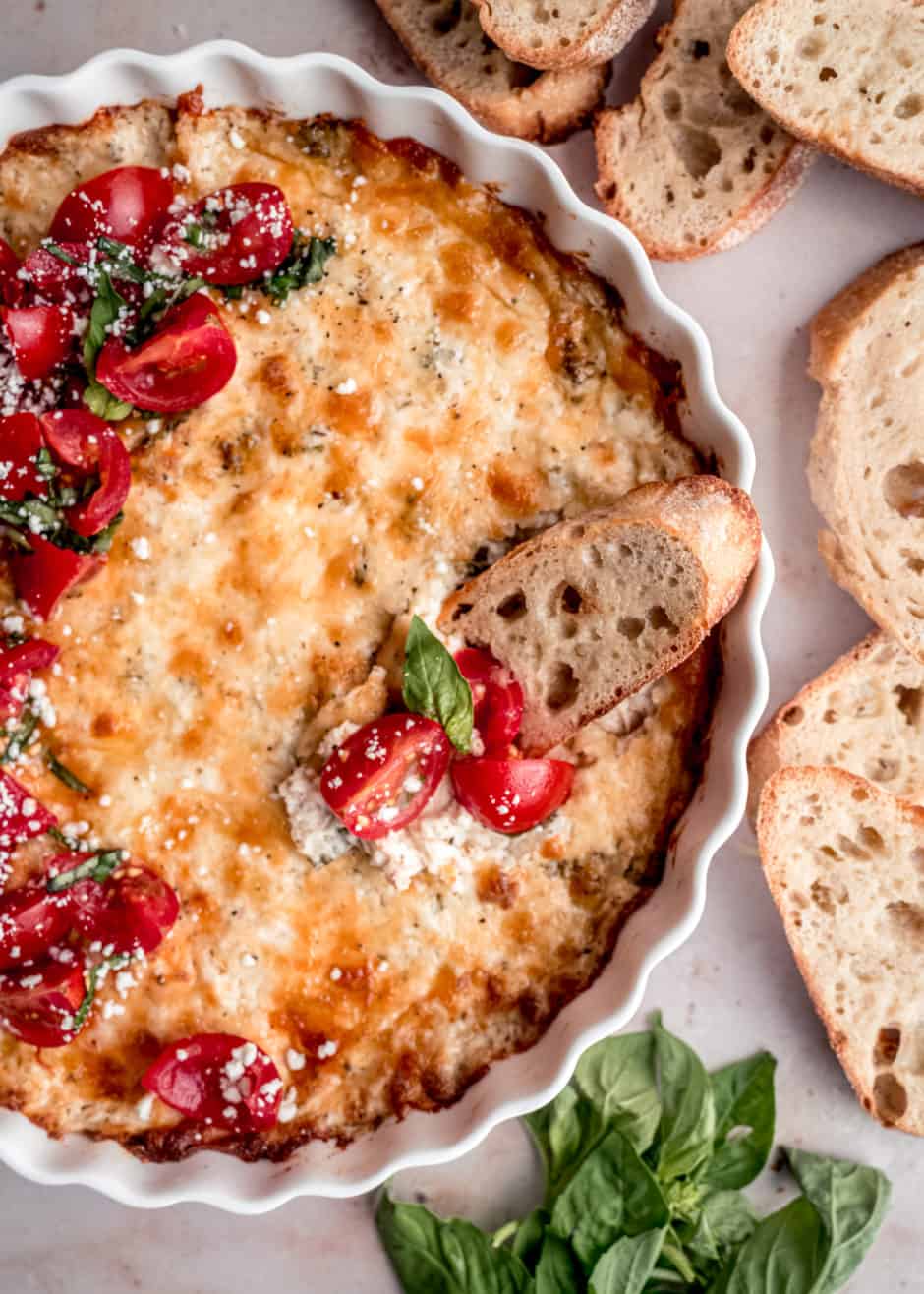 chicken alfredo dip with toasted slices of baguette and bruschetta tomatoes on top