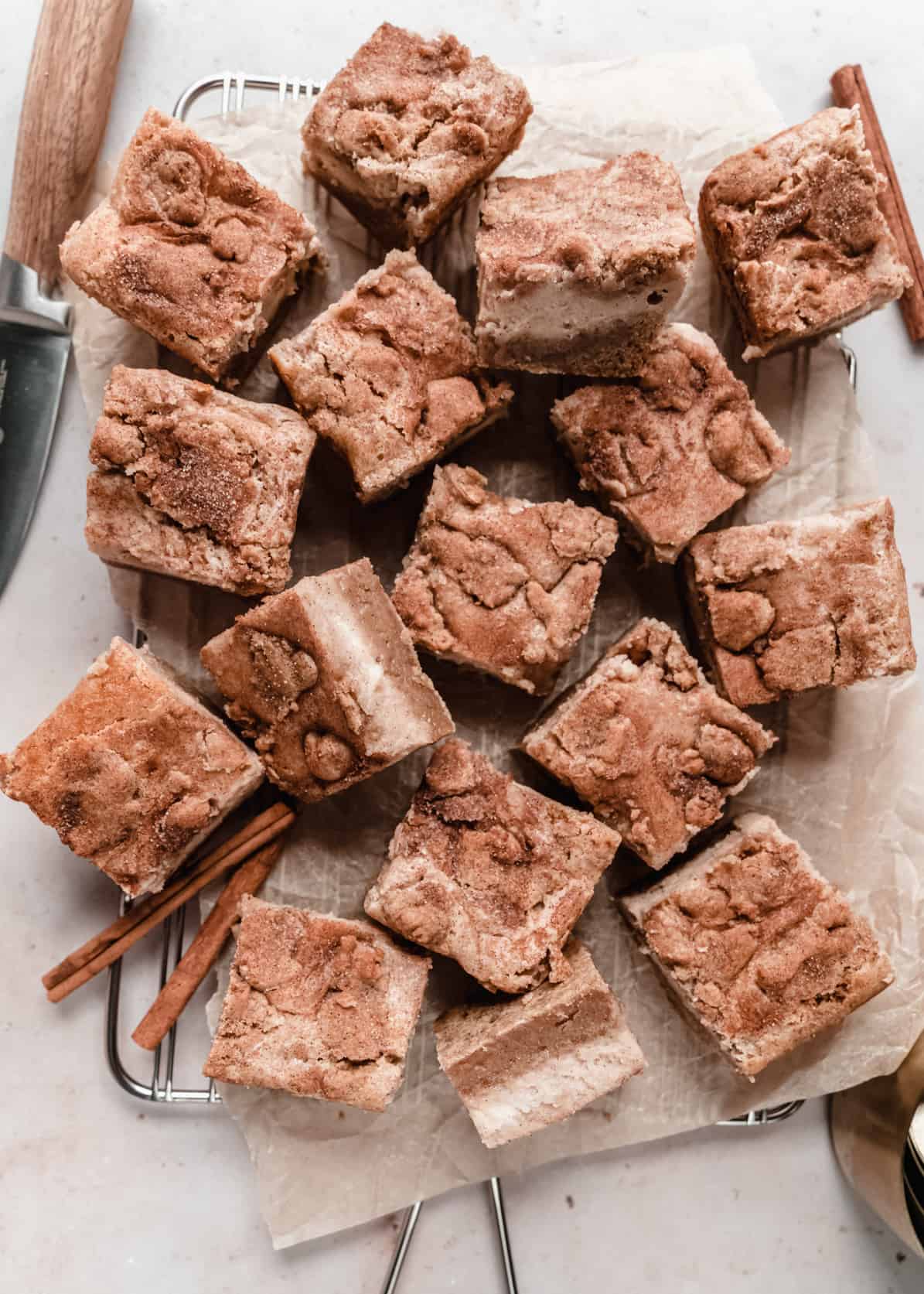 overhead shot of snickerdoodle cheesecake bars cut into squares on cooling rack and parchment paper