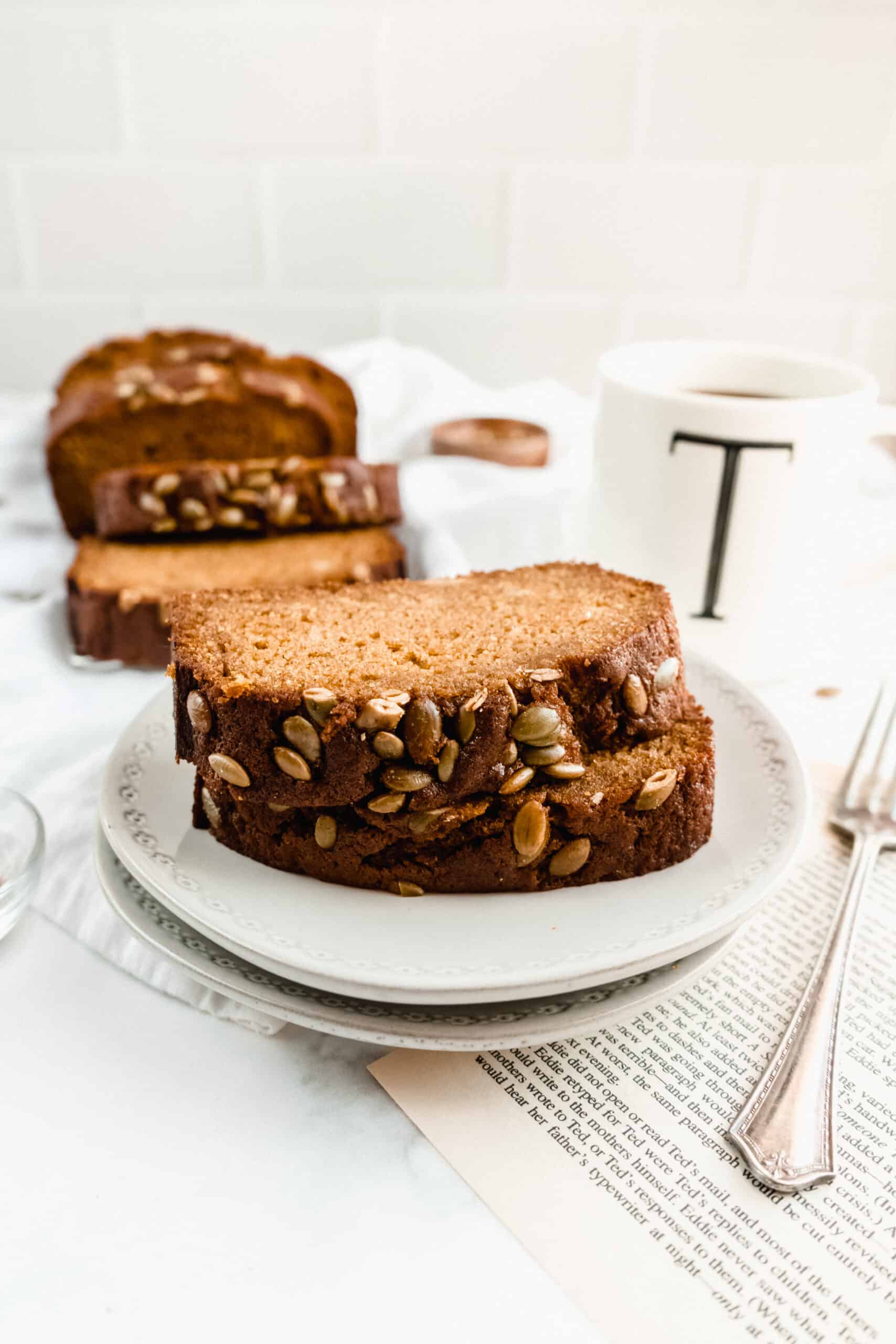 two slices of pumpkin bread on a stack of plates with a fork and cup of coffee in the background