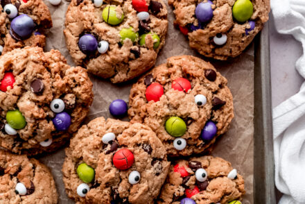halloween monster cookies on baking sheet with parchment paper and white cloth napkin on the right hand side