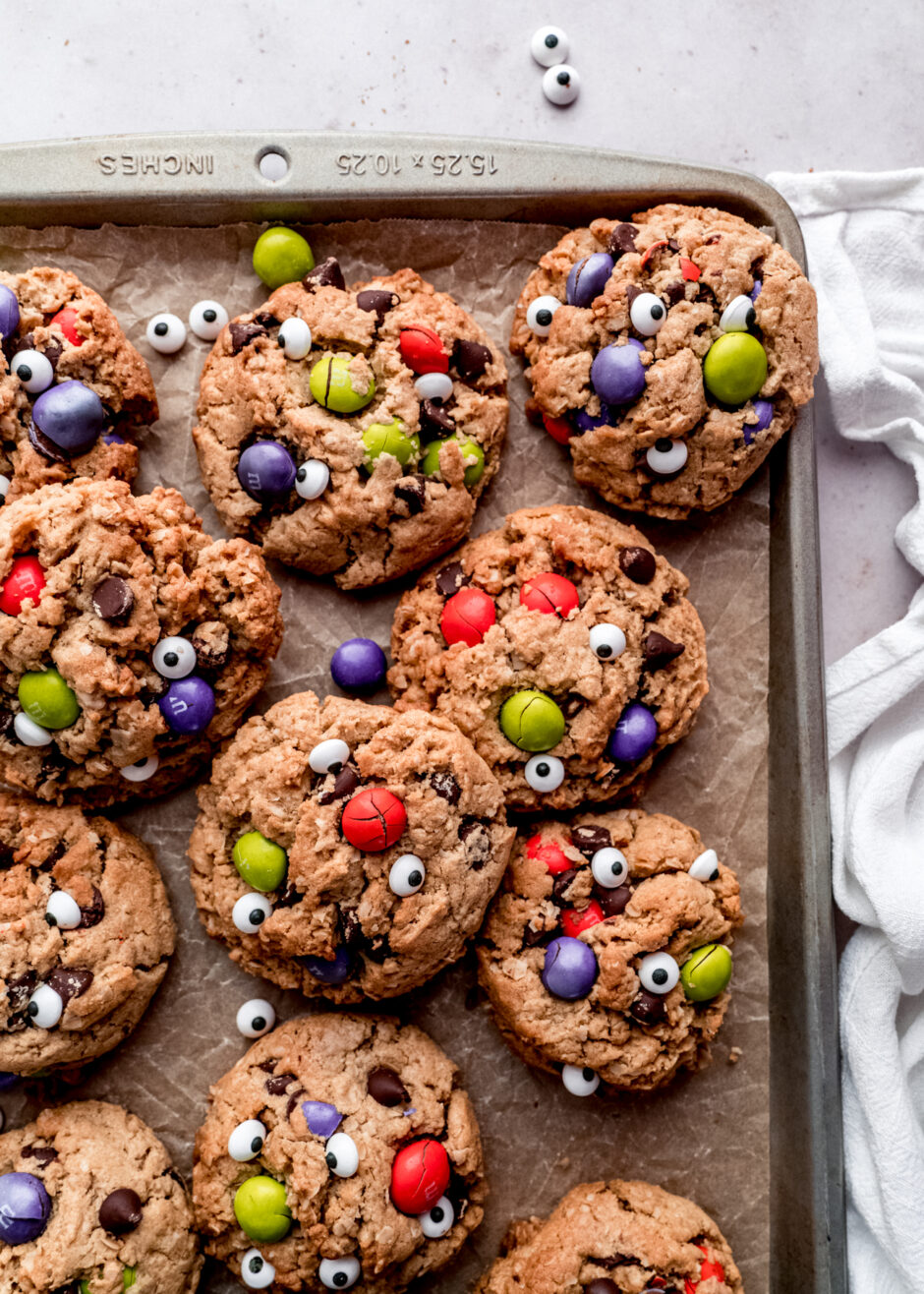 halloween monster cookies on baking sheet with parchment paper and white cloth napkin on the right hand side