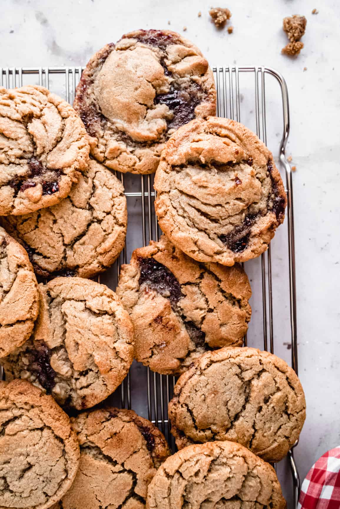 an overhead shot of a batch of peanut butter and jelly cookies cooling on a wire rack, with crackly golden-brown tops and swirls of dark jelly peeking through the soft, chewy centers.