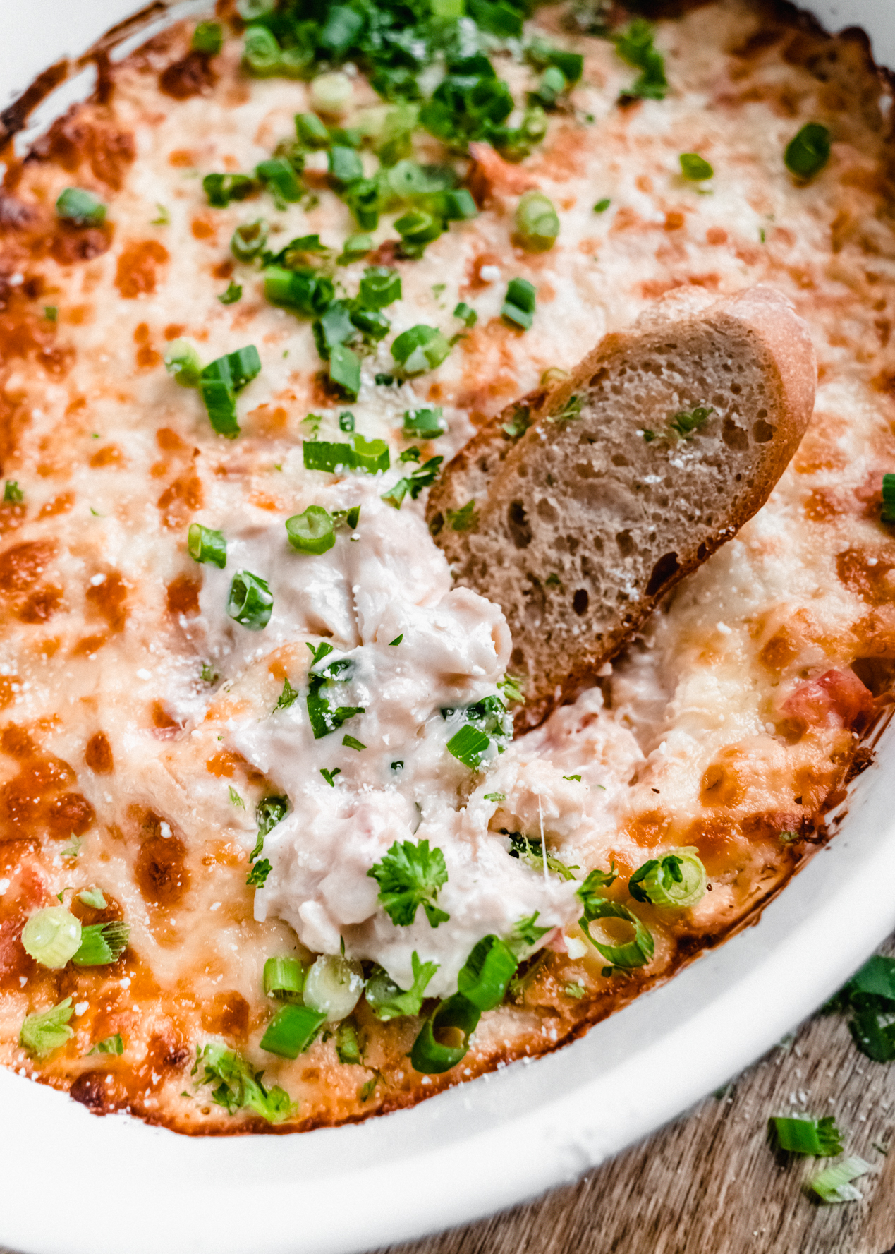 a toasted baguette slice sitting in baked crab rangoon dip in baking dish 