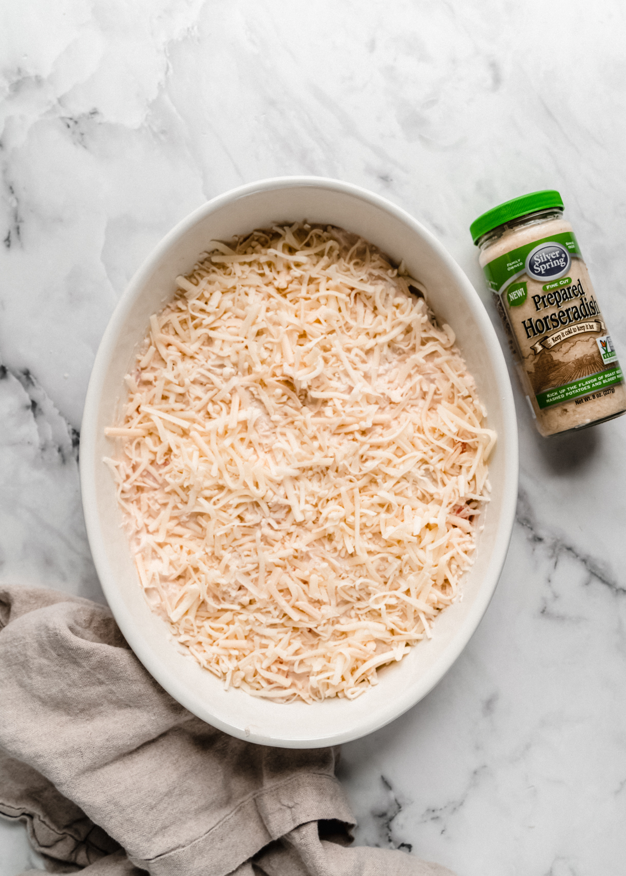 unbaked imitation crab dip in baking dish topped with cheese on marble counter 