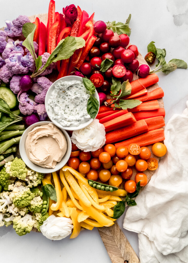 a close up shot of the red and orange sections of the crudité platter with cherry tomatoes, sliced carrots, sliced bell pepper