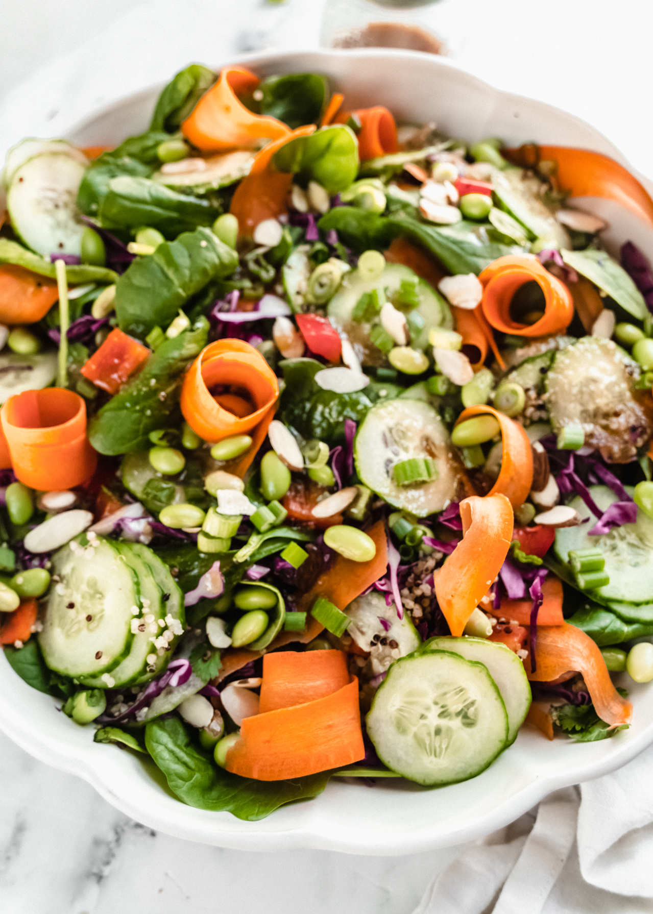 close up shot of dressed asian edamame salad with carrot ribbons in scalloped bowl