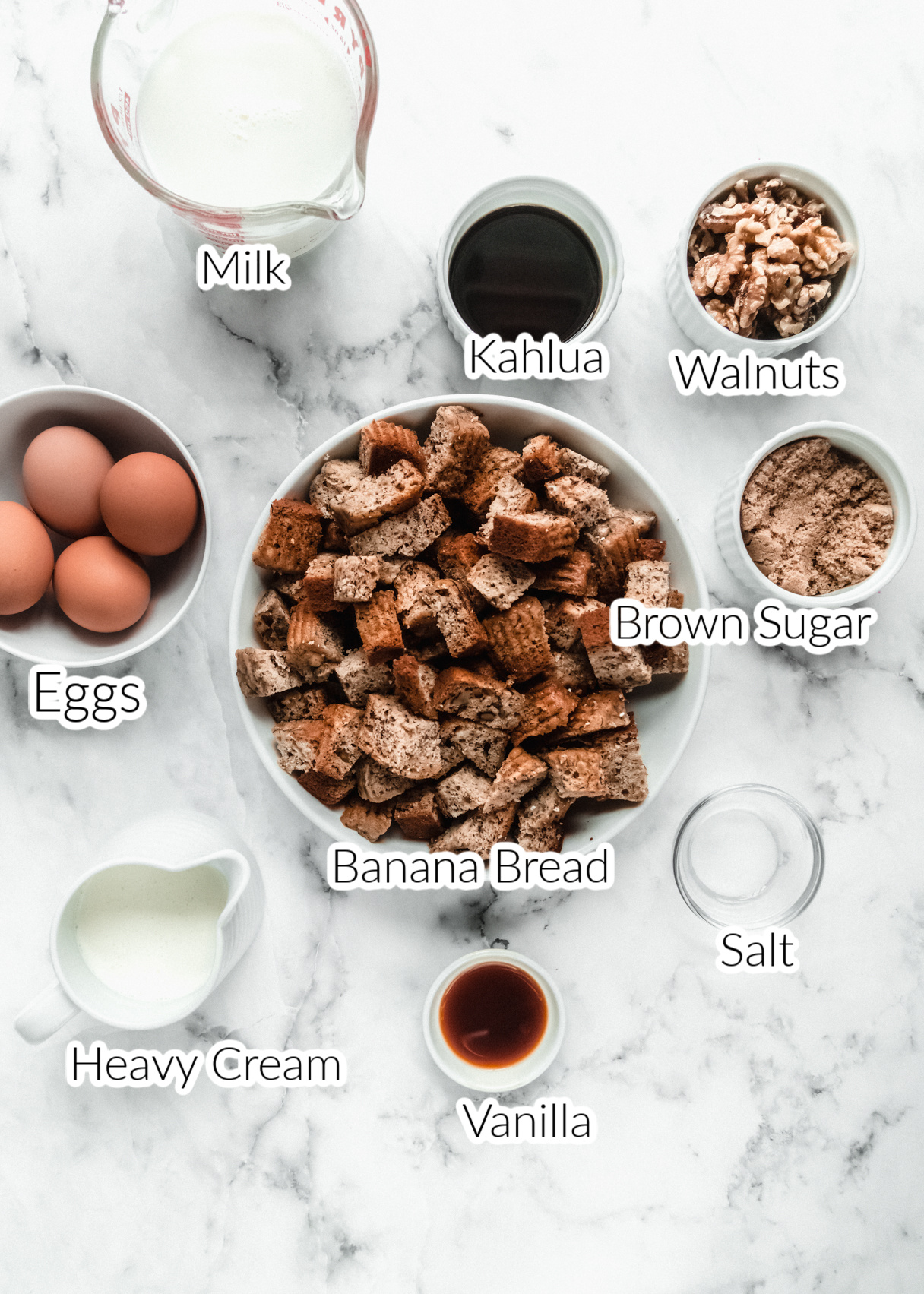 ingredients for banana bread bread pudding in individual bowls on marble backdrop