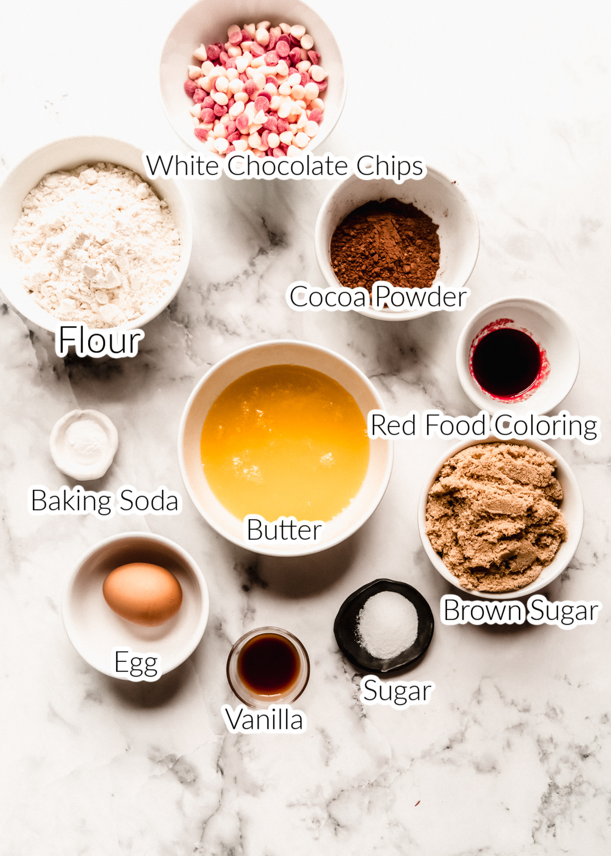 red velvet chocolate chip cookie ingredients in individual bowls on marble counter