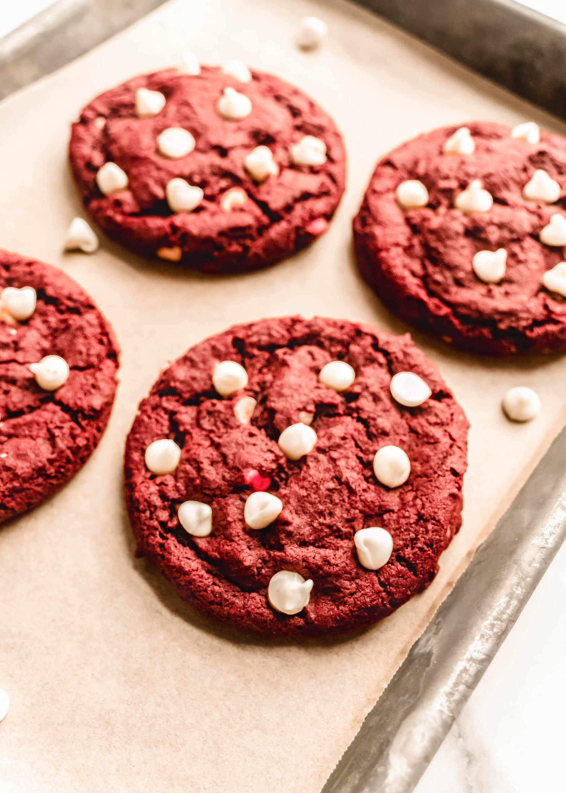 Close-up of freshly baked red velvet chocolate chip cookies topped with white chocolate chips on a parchment-lined baking sheet.