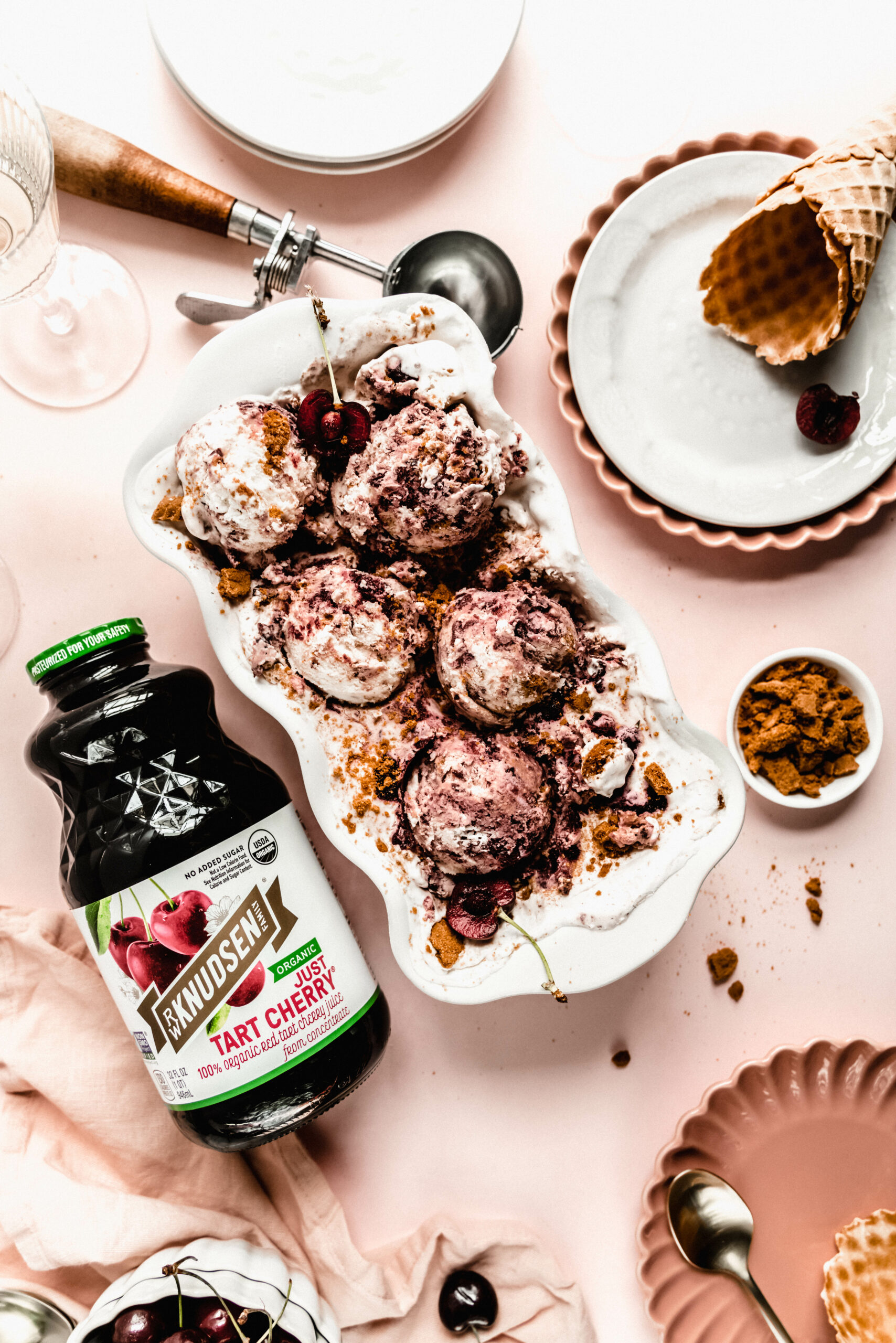 cherry cheesecake ice cream in white loaf pan with cherry juice jar laying next to it on a pink background.