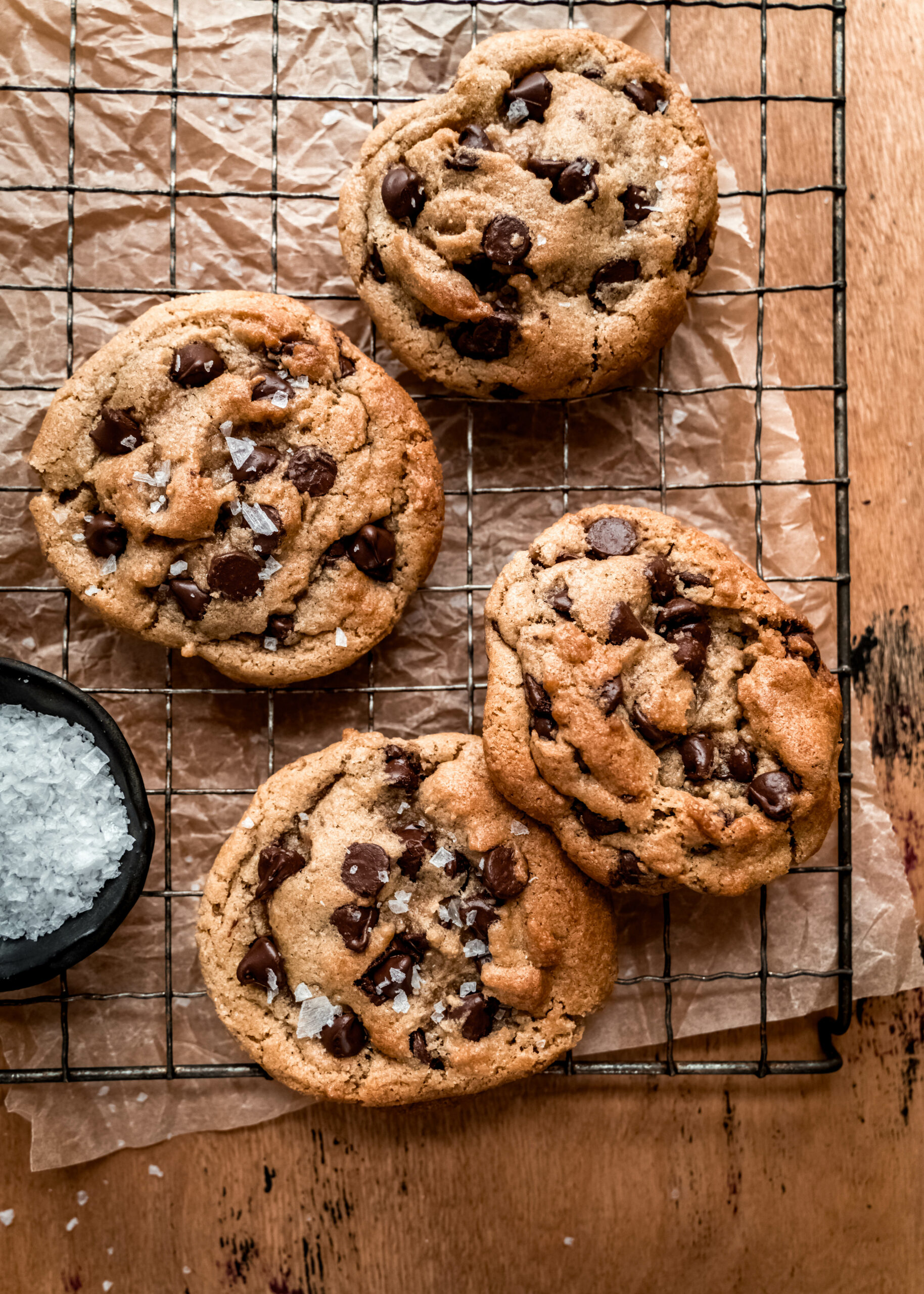 overhead shot of four chocolate chip cookies on cooling rack with brown parchment paper underneath